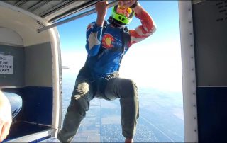 licensed skydiver hangs out of plane ready to jump